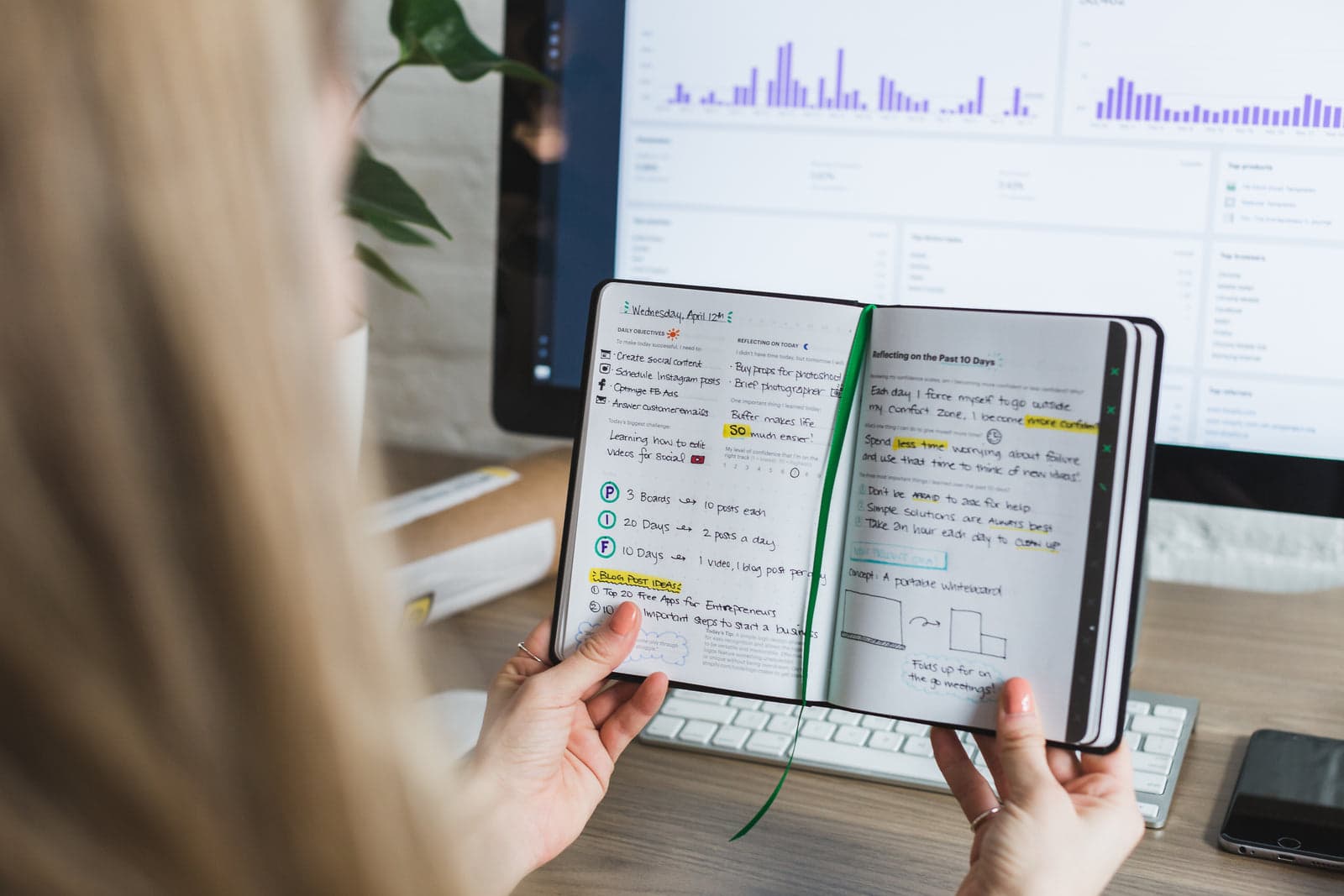 person taking notes beside a screen of charts