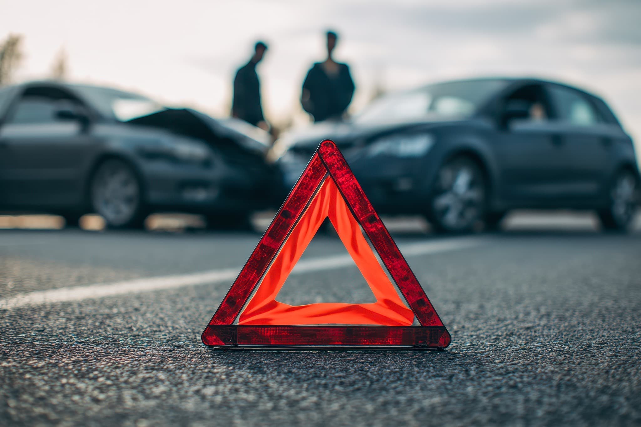 Red warning triangle on the road in front of two cars after a collision