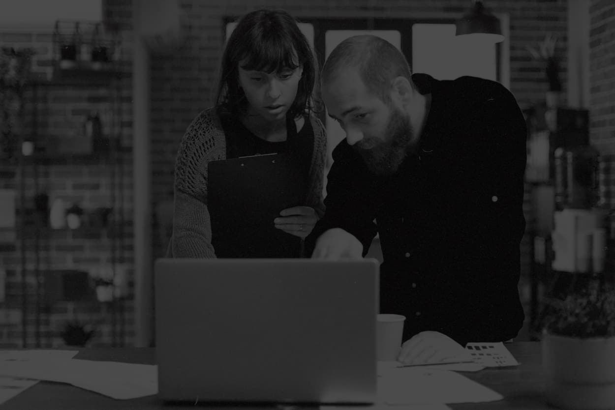 Two colleagues reviewing work together at a laptop, in muted monochrome