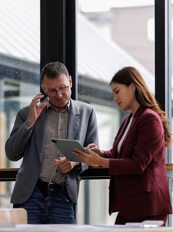 Two colleagues reviewing information on a tablet by an office window