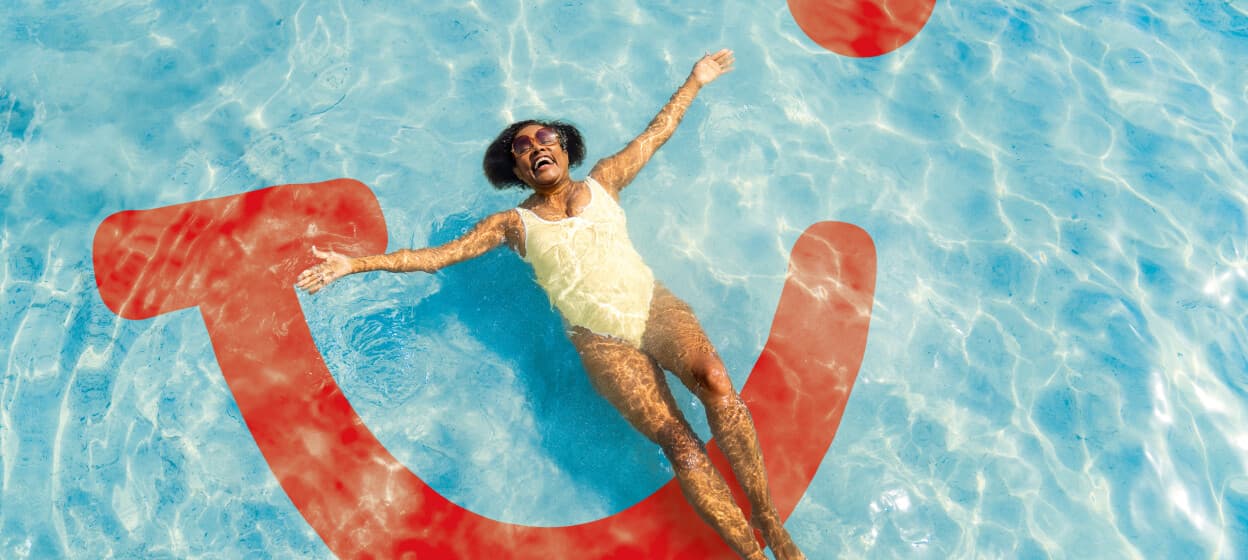 Woman floating on her back in a swimming pool beside a large red TUI smile logo