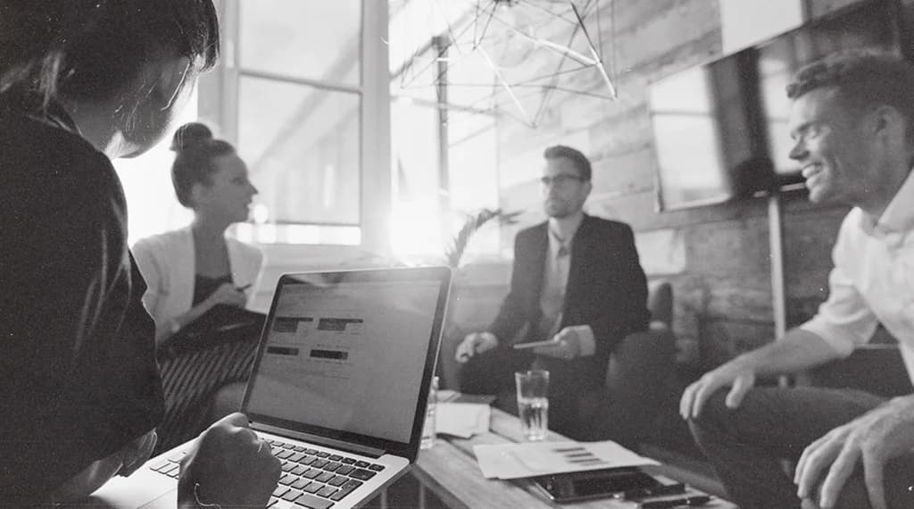 Team meeting around a laptop in a bright office, in black and white